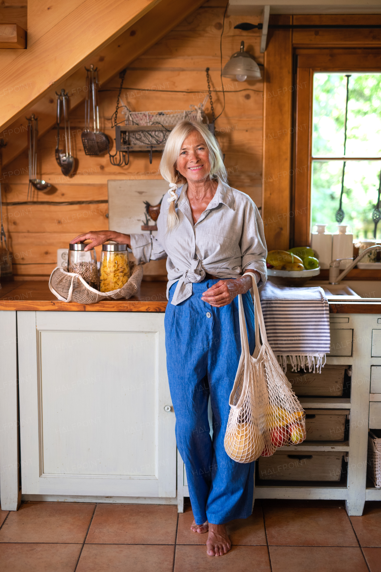 A happy senior woman unpacking shopping indoors at home and looking at camera, sustainable lifestyle.