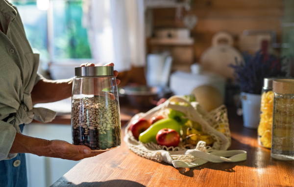 A close-up of senior woman unpacking local food in zero waste packaging from bag in kitchen at home.