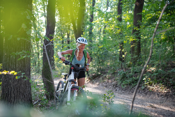 An active senior woman biker pushing ebike outdoors in forest.