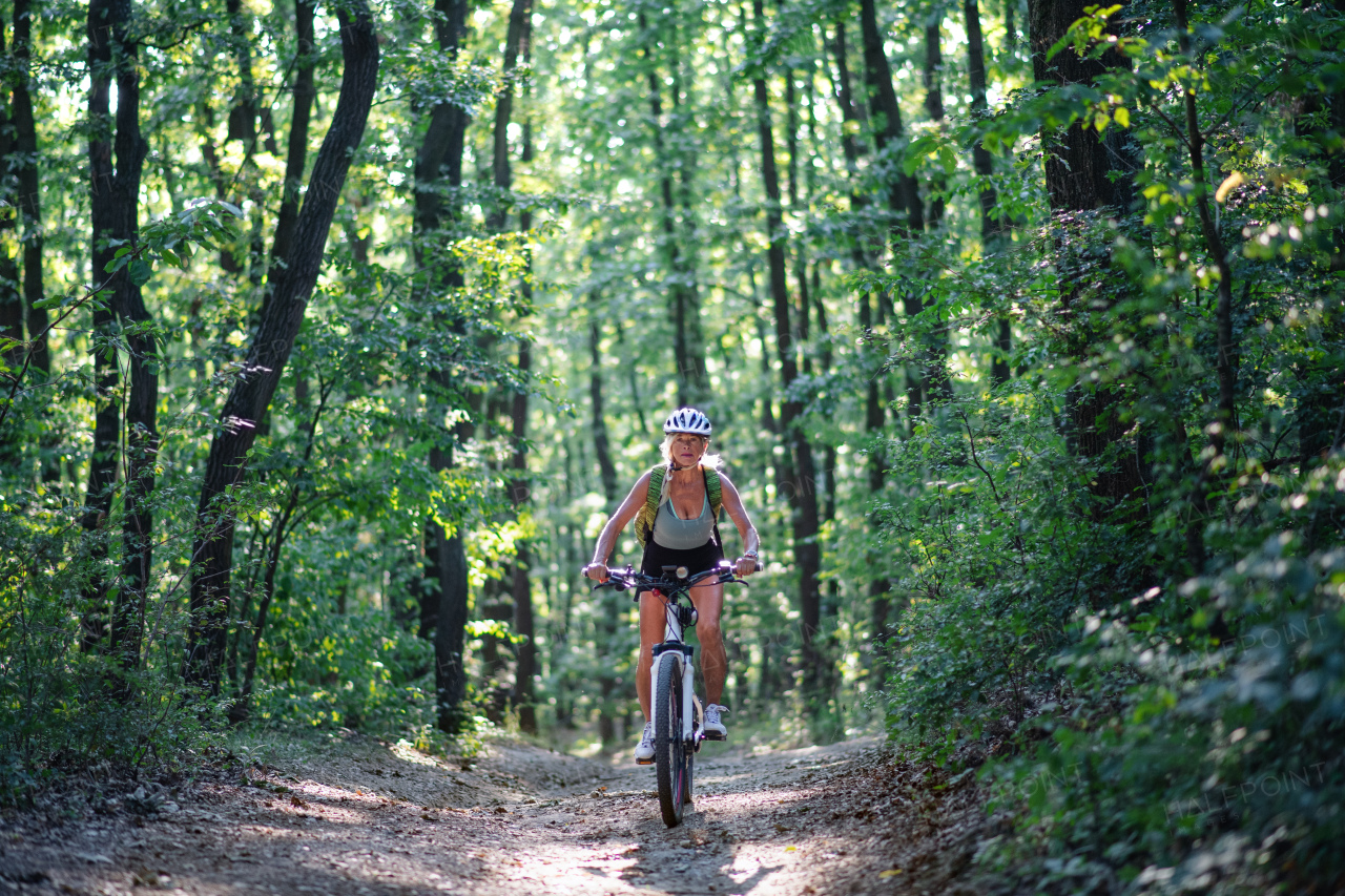 A front view of active senior woman biker cycling outdoors in forest.