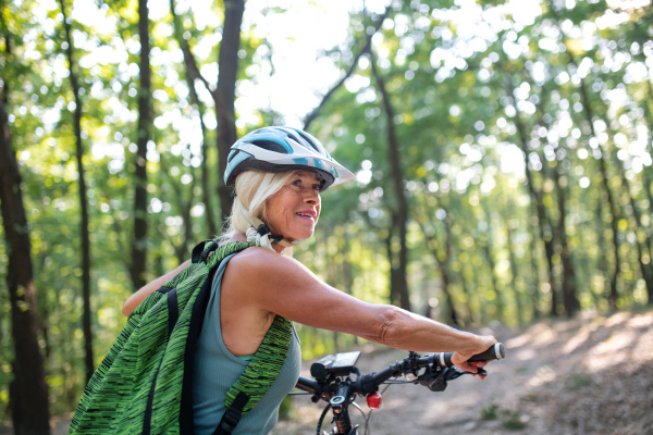 An active senior woman biker pushing bike outdoors in forest.