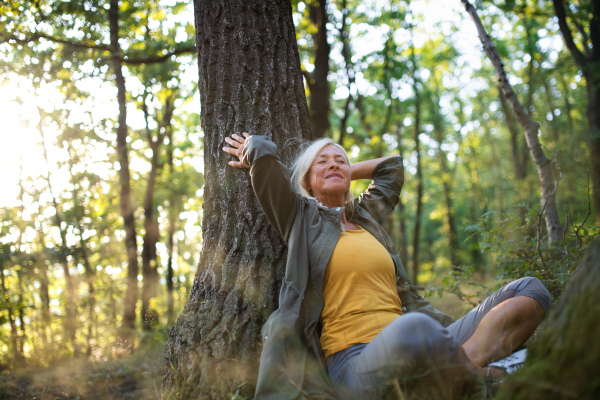 A portrait of senior woman relaxing and sitting with eyes closed outdoors in forest.