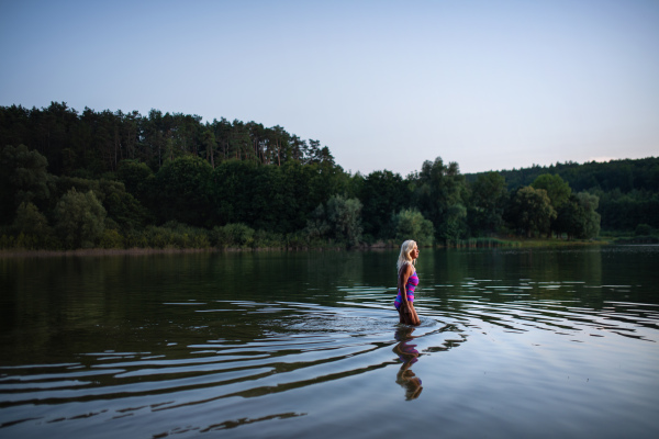 A side view of active senior woman swimmer diving outdoors in lake.