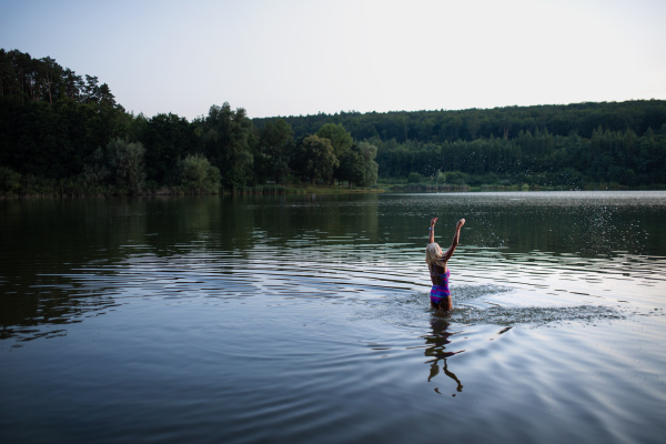 A portrait of active senior woman swimmer standing and stretching outdoors in lake.