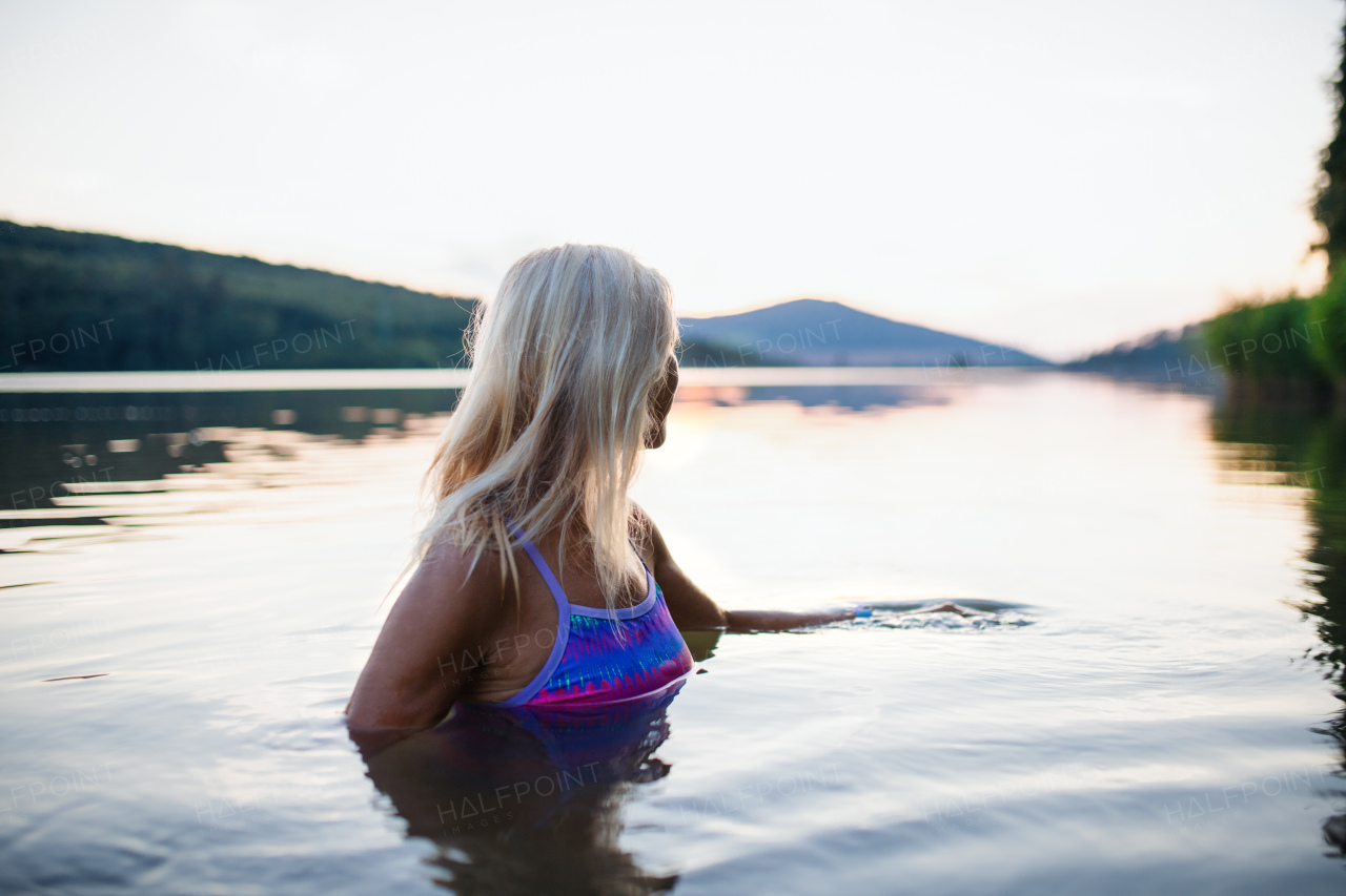 A side view of active senior woman swimmer diving outdoors in lake.