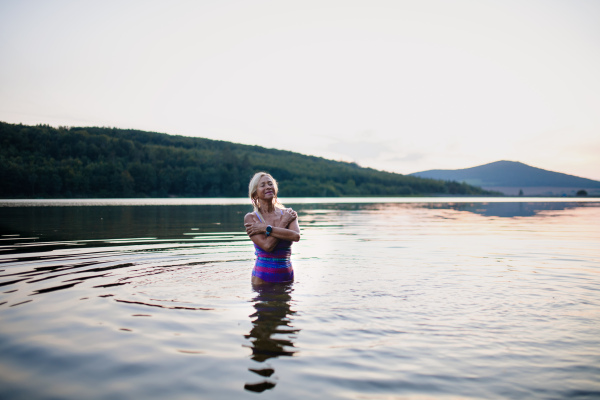 A portrait of active senior woman swimmer standing and splashing outdoors in lake.