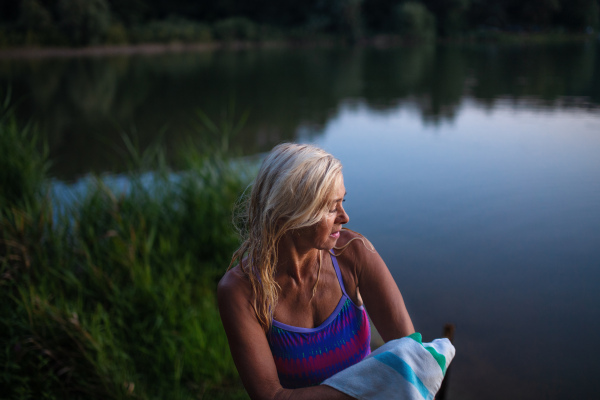 A portrait of active senior woman swimmer drying herself with towell outdoors by lake.