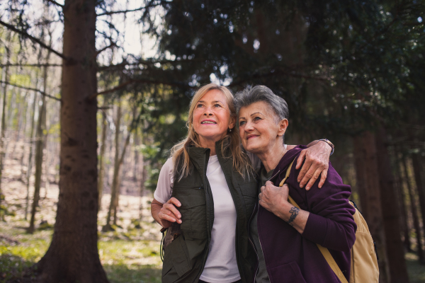 Happy senior women hikers outdoors walking in forest in nature, talking.