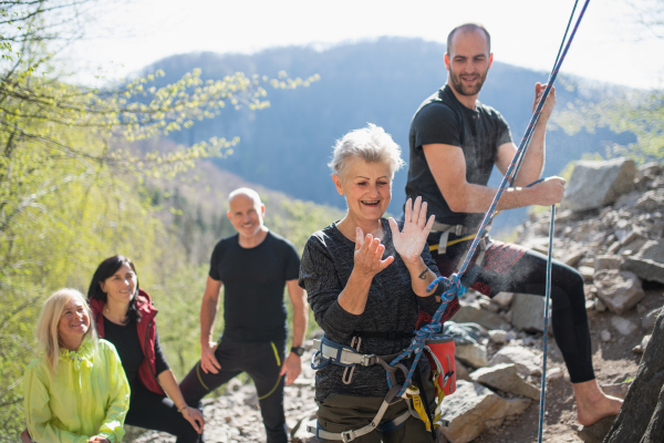 A group of seniors with instructor using chalk before climbing rocks outdoors in nature, active lifestyle.