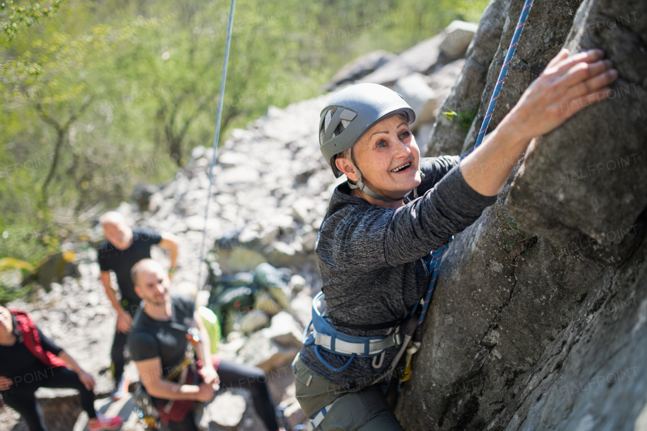 A group of seniors with instructor climbing rocks outdoors in nature, active lifestyle.