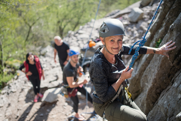 A group of seniors with instructor climbing rocks outdoors in nature, active lifestyle.