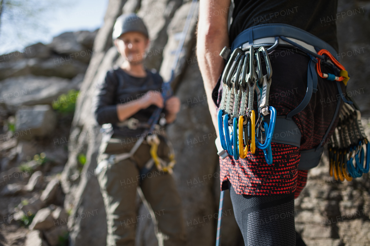 An unrecognizable instructor with harness and carabiners climbing rocks with seniors outdoors in nature, active lifestyle.