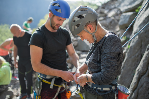 A group of seniors with instructor climbing rocks outdoors in nature, active lifestyle.