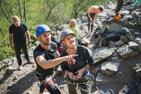 A group of seniors with instructor climbing rocks outdoors in nature, active lifestyle.