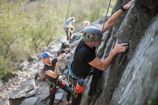 Portrait of senior man with instructor climbing rocks outdoors in nature, active lifestyle.