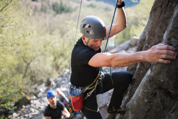 Portrait of senior man with instructor climbing rocks outdoors in nature, active lifestyle.