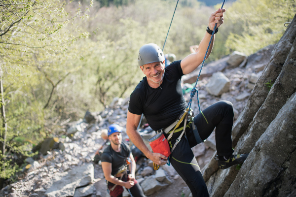 Portrait of senior man with instructor climbing rocks outdoors in nature, active lifestyle.