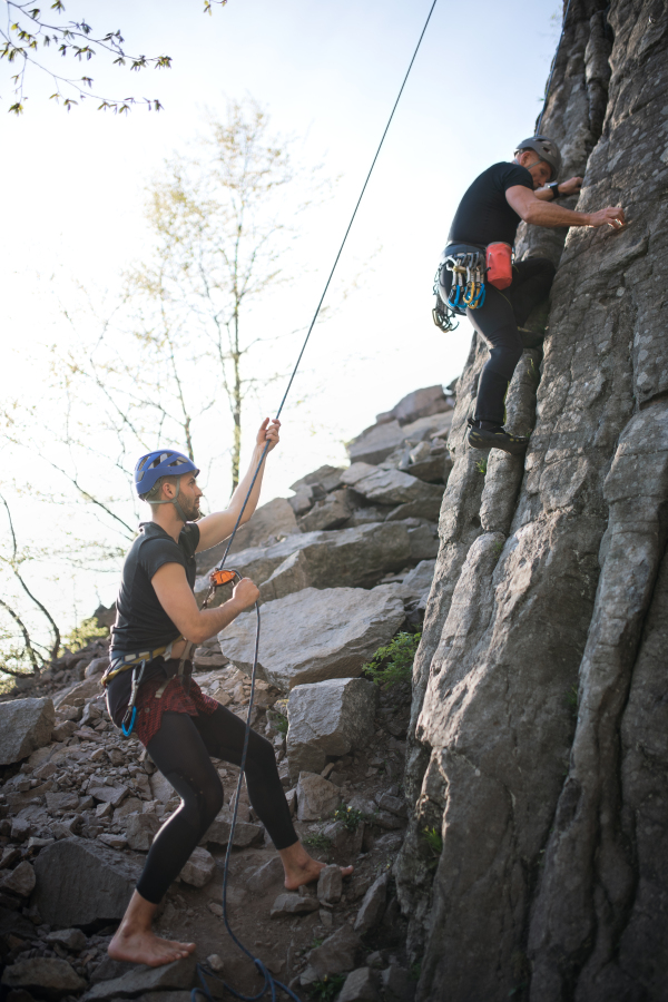 Portrait of senior man with instructor climbing rocks outdoors in nature, active lifestyle.