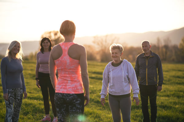 A group of seniors with sport instructor doing exercise outdoors in nature at sunset, active lifestyle.