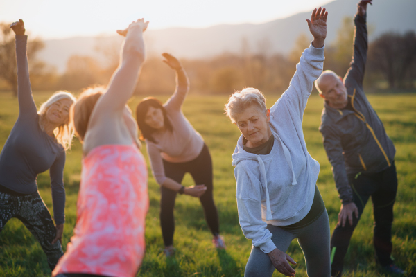 A group of seniors with sport instructor doing exercise outdoors in nature at sunset, active lifestyle.