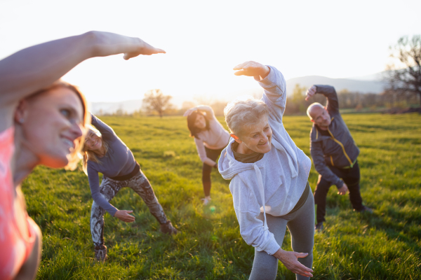 A group of seniors with sport instructor doing exercise outdoors in nature at sunset, active lifestyle.