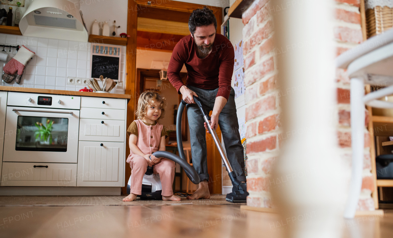 A father with small daughter hoovering indoors at home, daily chores concept.