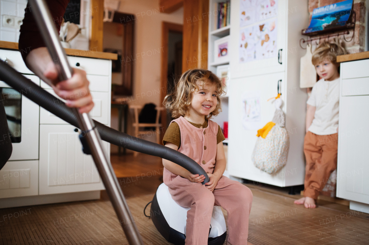 An unrecognizable father with small children hoovering indoors at home, daily chores concept.