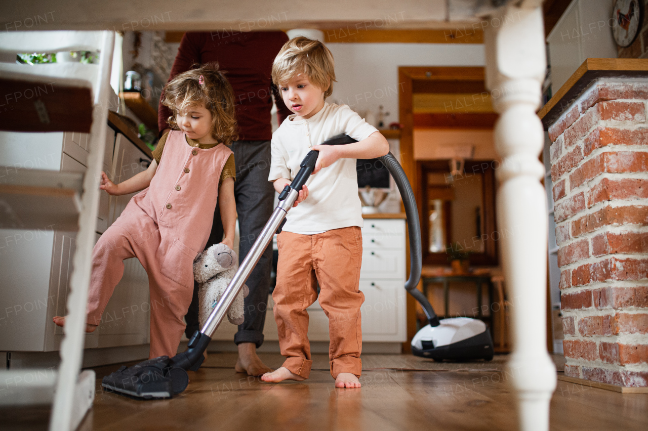 An unrecognizable father with two small children hoovering indoors at home, housework concept.