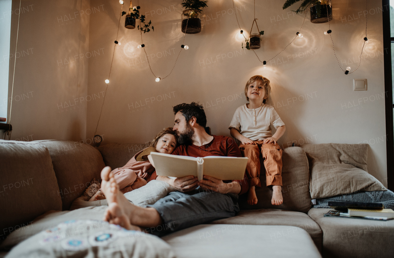 A mature father with two small children resting indoors at home, looking at photo album.