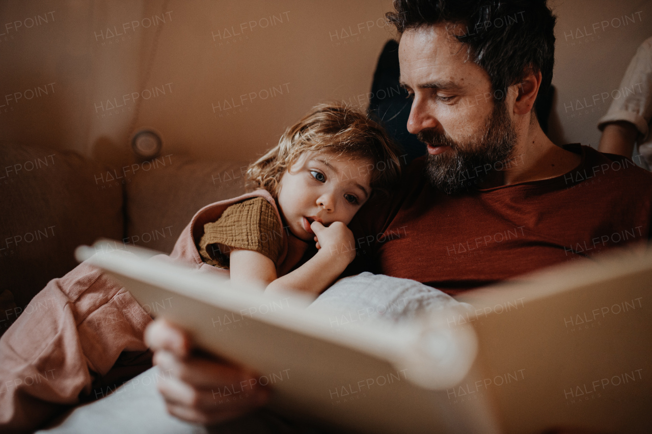 A mature father with small daughter resting indoors at home, looking at photo album.