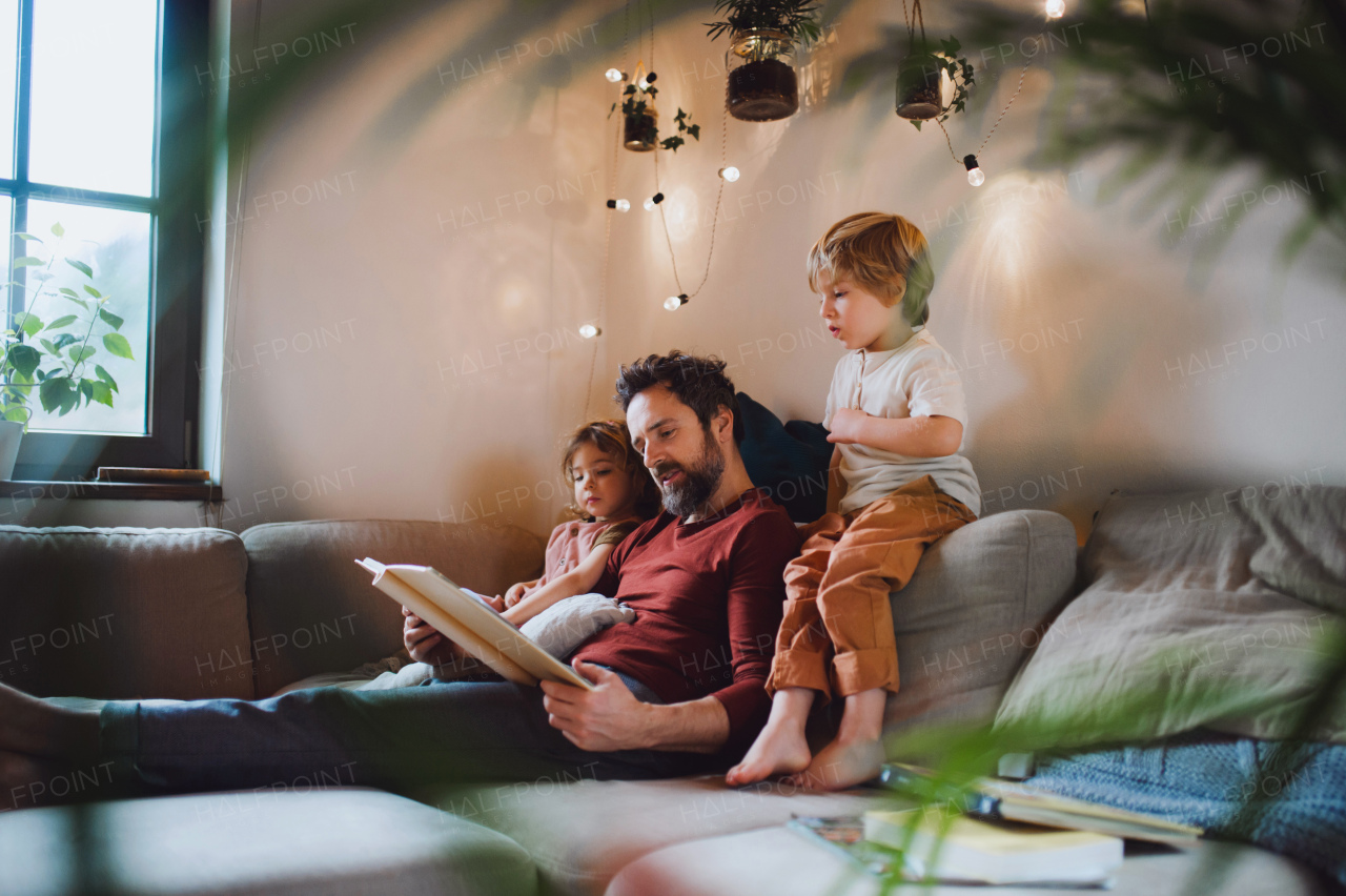 A mature father with two small children resting indoors at home, looking at photo album.