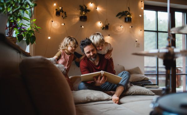 A mature father with two small children resting indoors at home, looking at photo album.