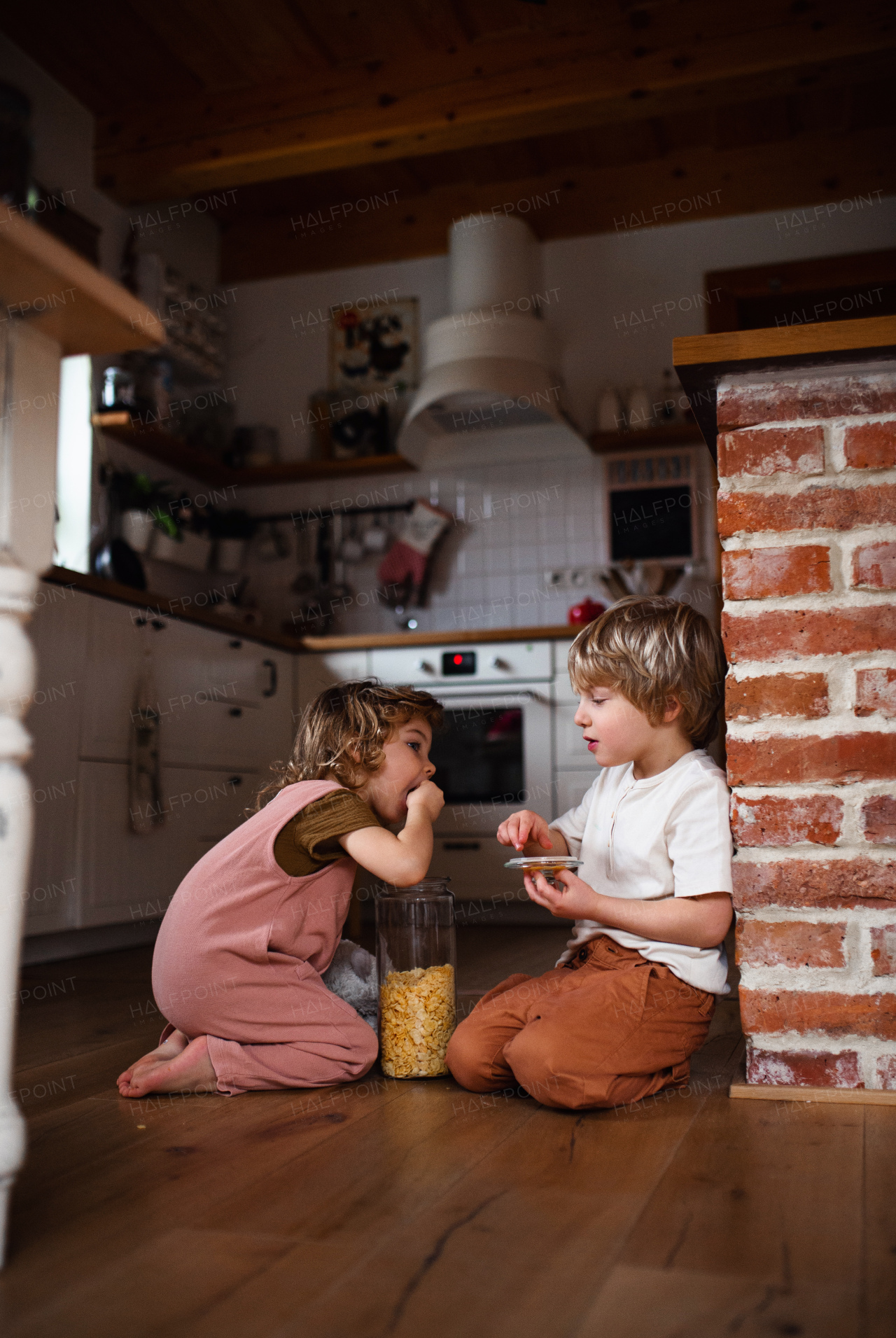 Two happy small children indoors at home, eating cornflakes on floor.