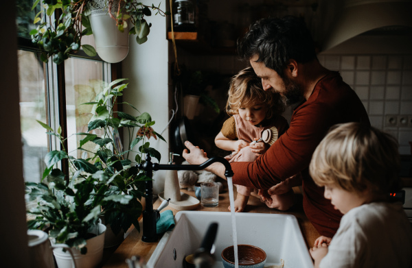 A mature father with two small children washing dishes indoors at home, daily chores concept.