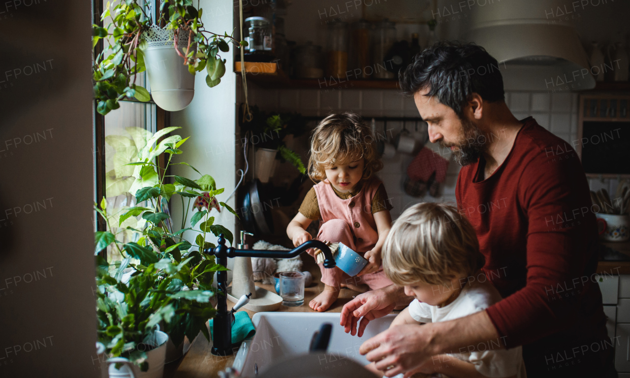 A mature father with two small children washing dishes indoors at home, daily chores concept.