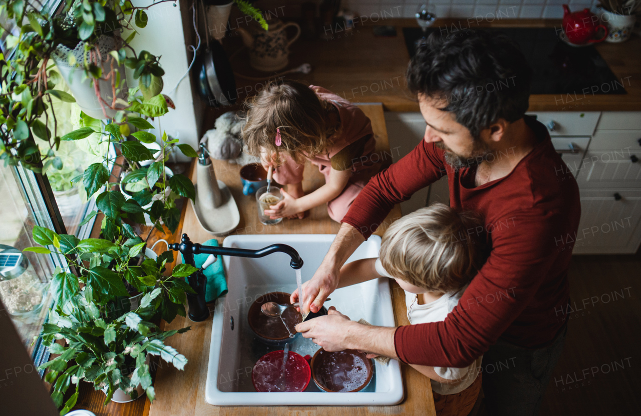 A top view of father with two small children washing dishes indoors at home, daily chores concept.