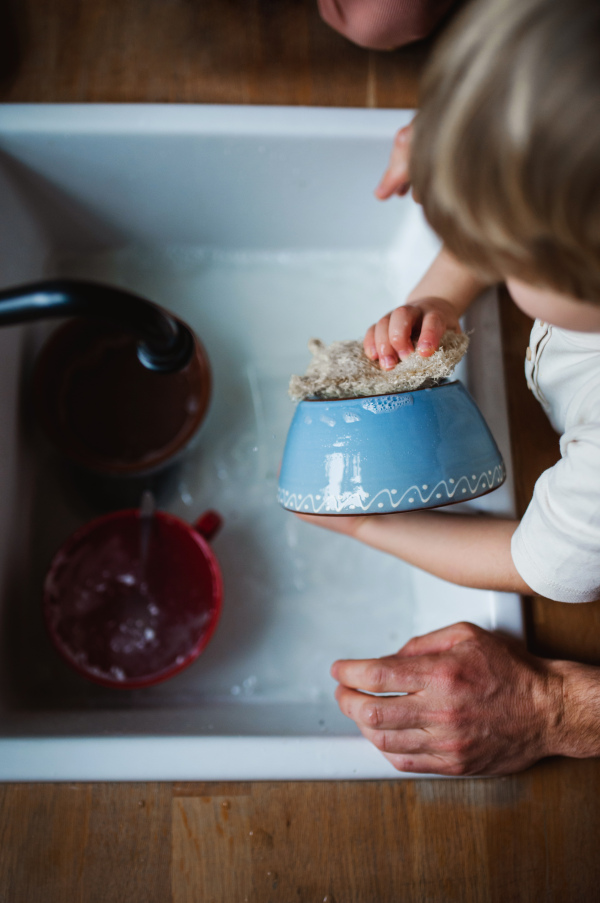 A top view of small boy with father washing dishes indoors at home, daily chores concept.