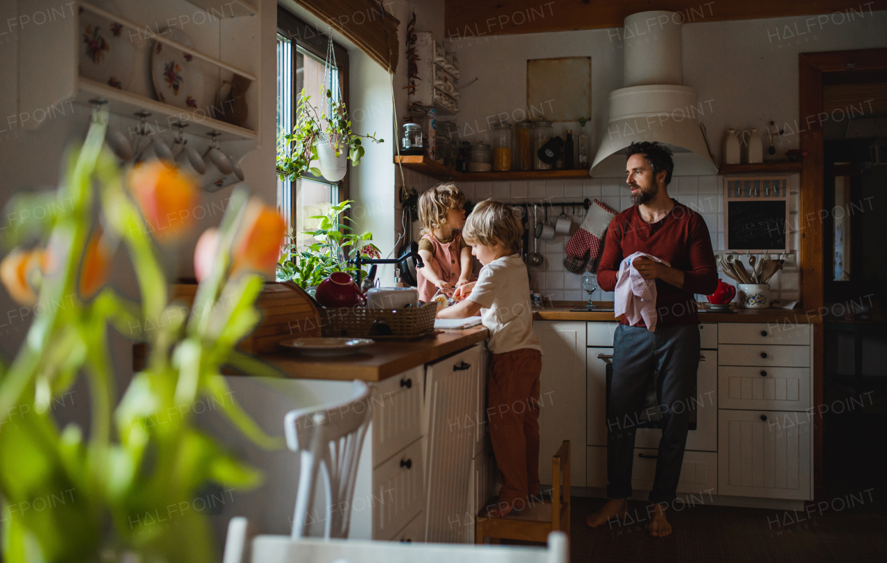 A mature father with two small children washing dishes indoors at home, daily chores concept.