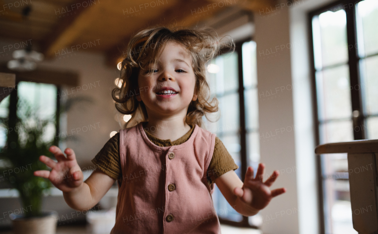 A happy small girl jumping at home, looking at camera.