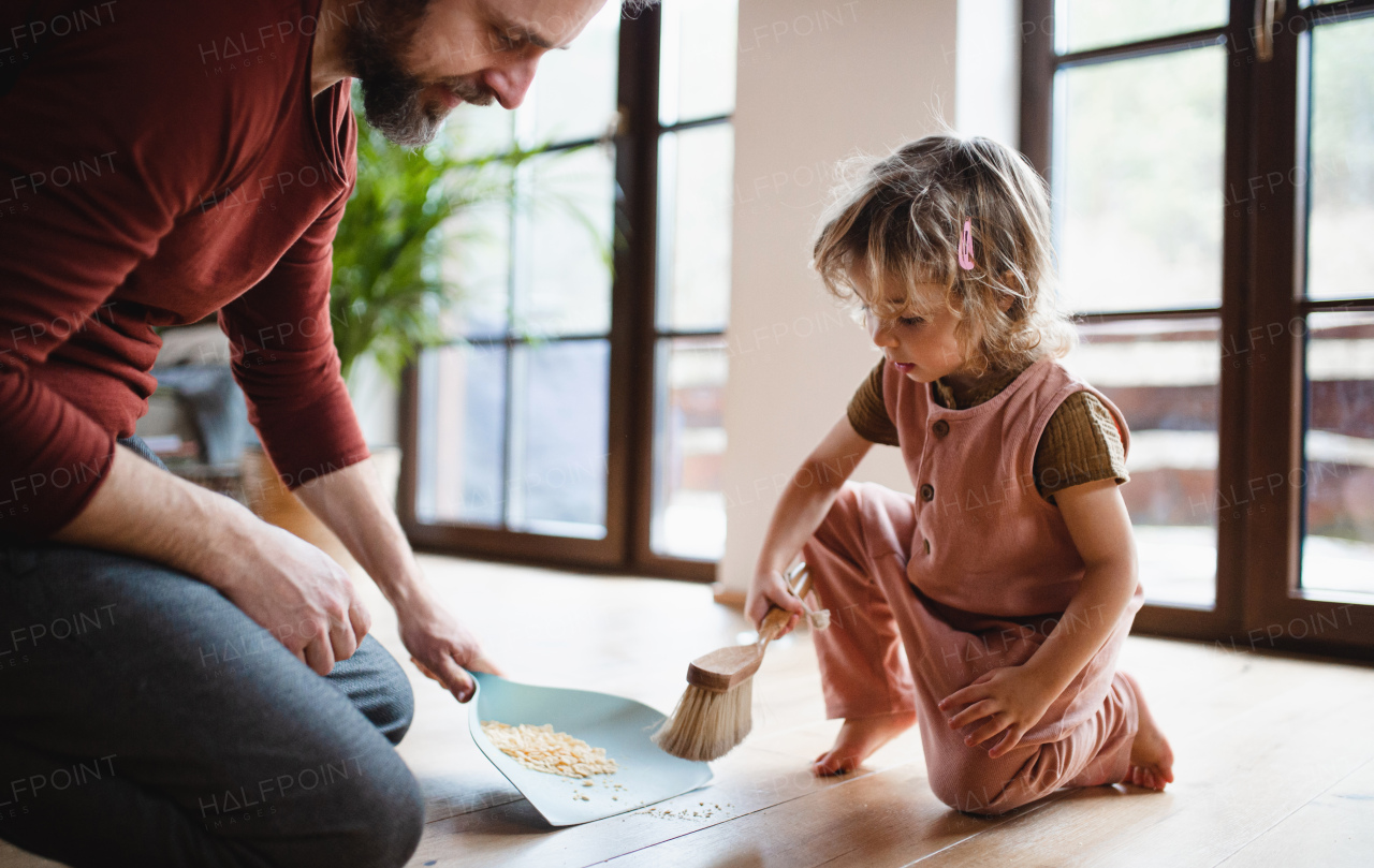 Mid adult father with a small daughter sweeping cornflakes at home, daily chores concept.