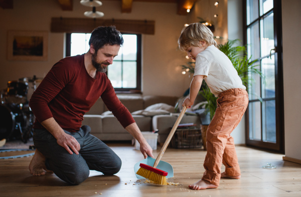 Father with a small son sweeping at home, daily chores concept.