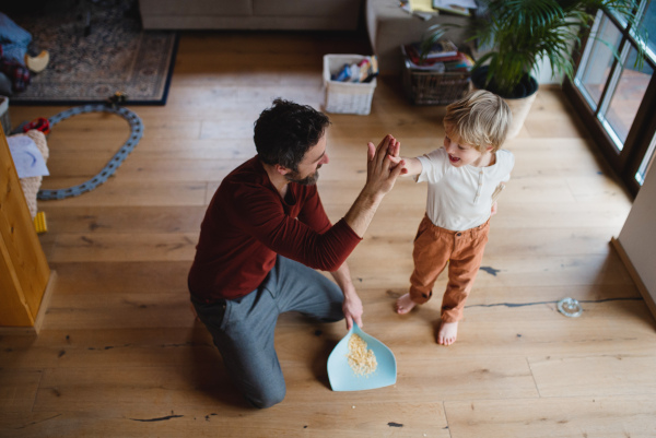 High anlge view of a father high fiving with small son after sweeping at home, daily chores concept.