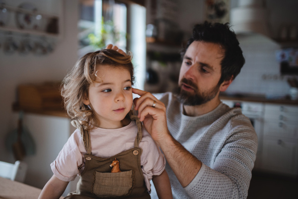 A mature father with small daugther resting indoors at home and combing hair.