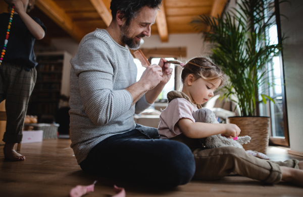 A mature father with small son and daugther resting indoors at home, playing and combing hair.