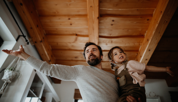 Low angle view of a mature father with small daughter standing indoors at home, holding and hugging.