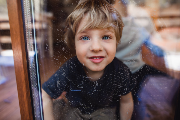 A happy boy with unrecognizable father cleaning windows at home, daily chores concept.