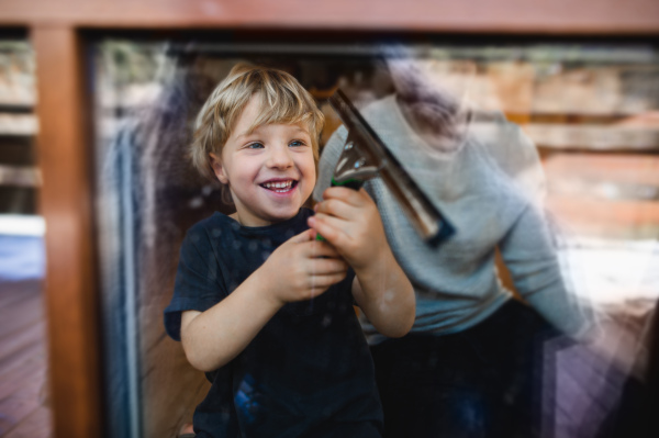 A happy boy with unrecognizable father cleaning windows at home, housework concept.