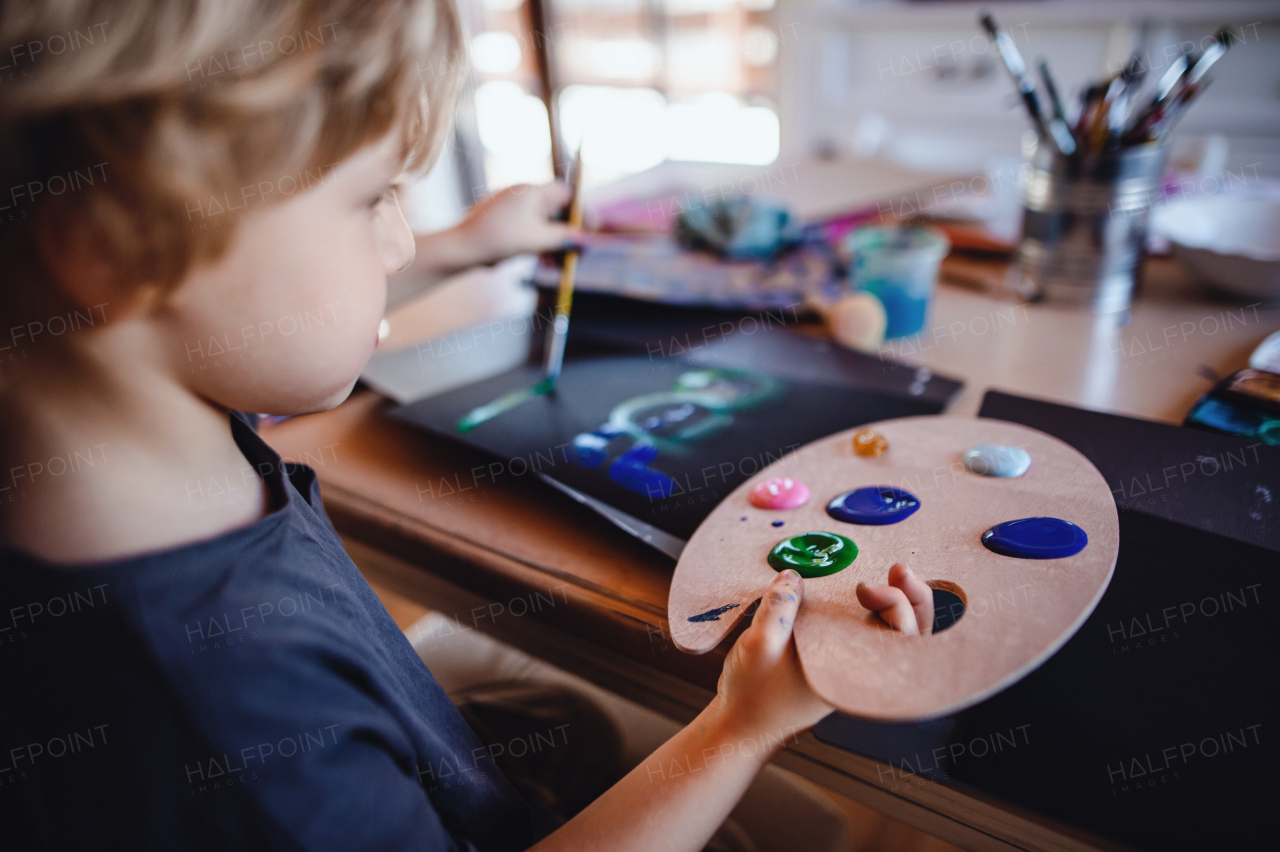 A concentrated small boy painting pictures indoors at home, leisure time