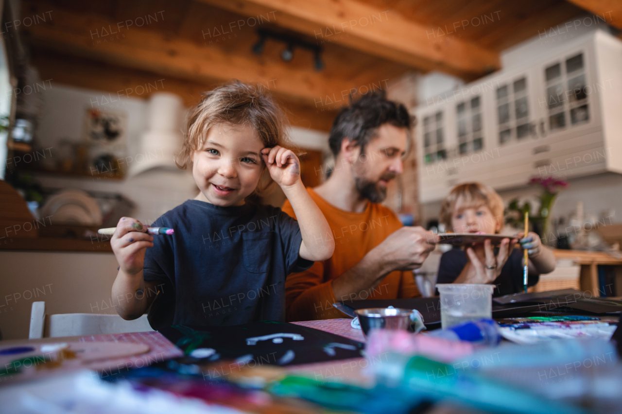 A mature father with two small children resting indoors at home, painting pictures.