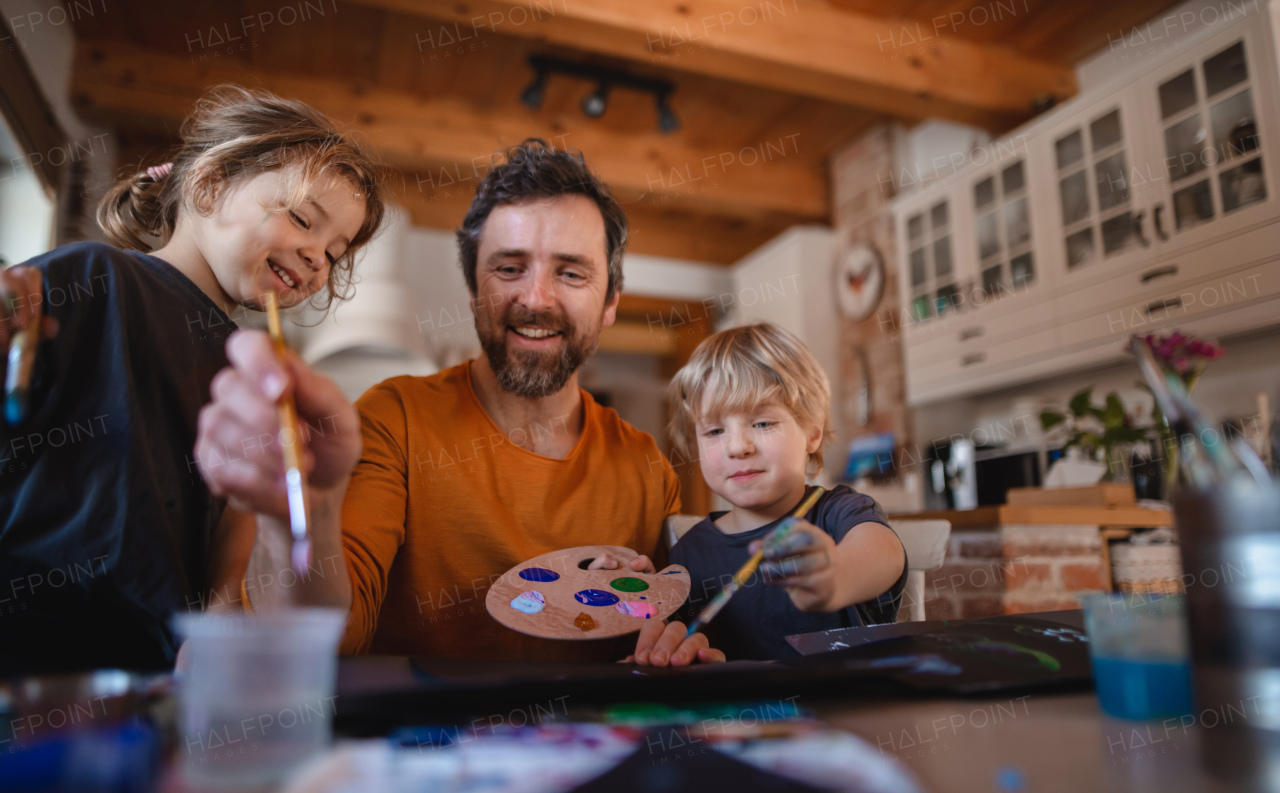 A mature father with two small children resting indoors at home, painting pictures.